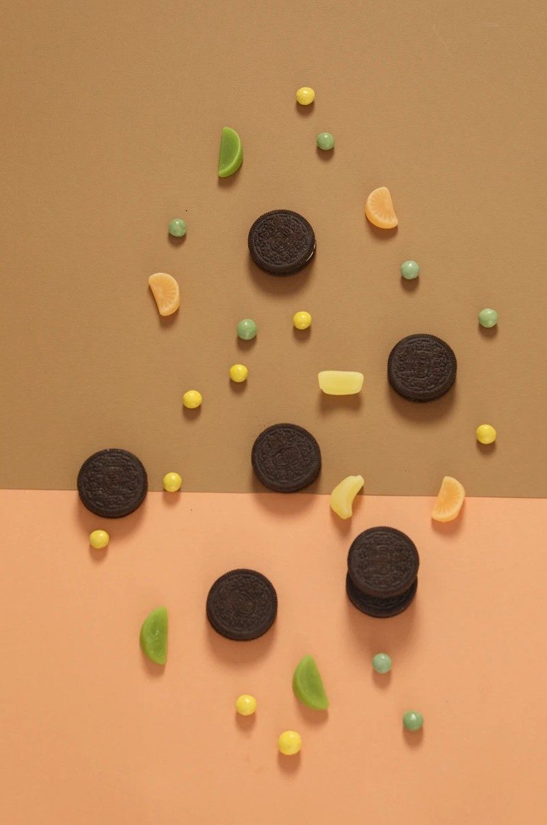 Dunkle runde Kekse und bunte Bonbons verteilt auf oliv-apricotfarbenem Hintergrund