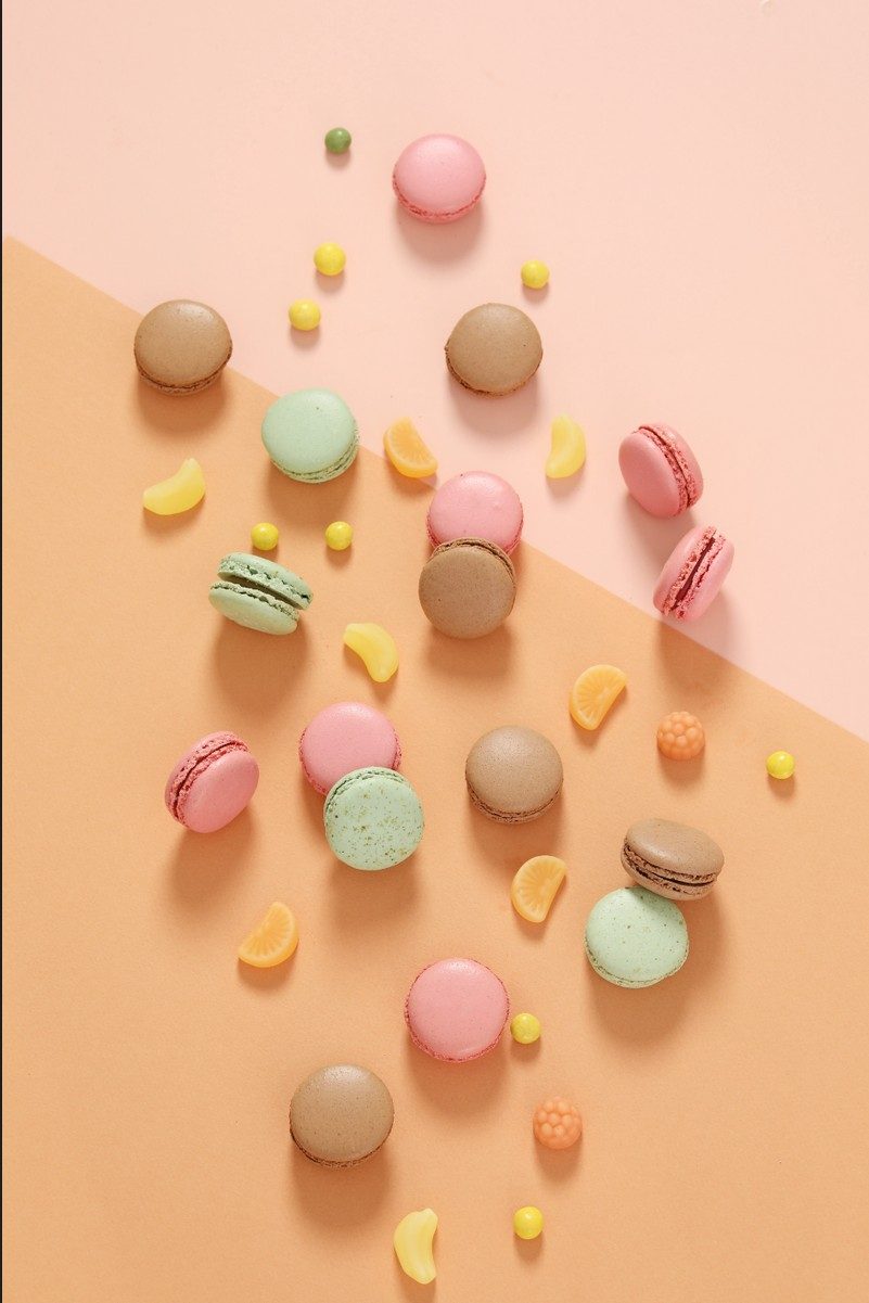 Flatlay mit pastellfarbenen Macarons und Bonbons auf rosa und apricotfarbenem Hintergrund