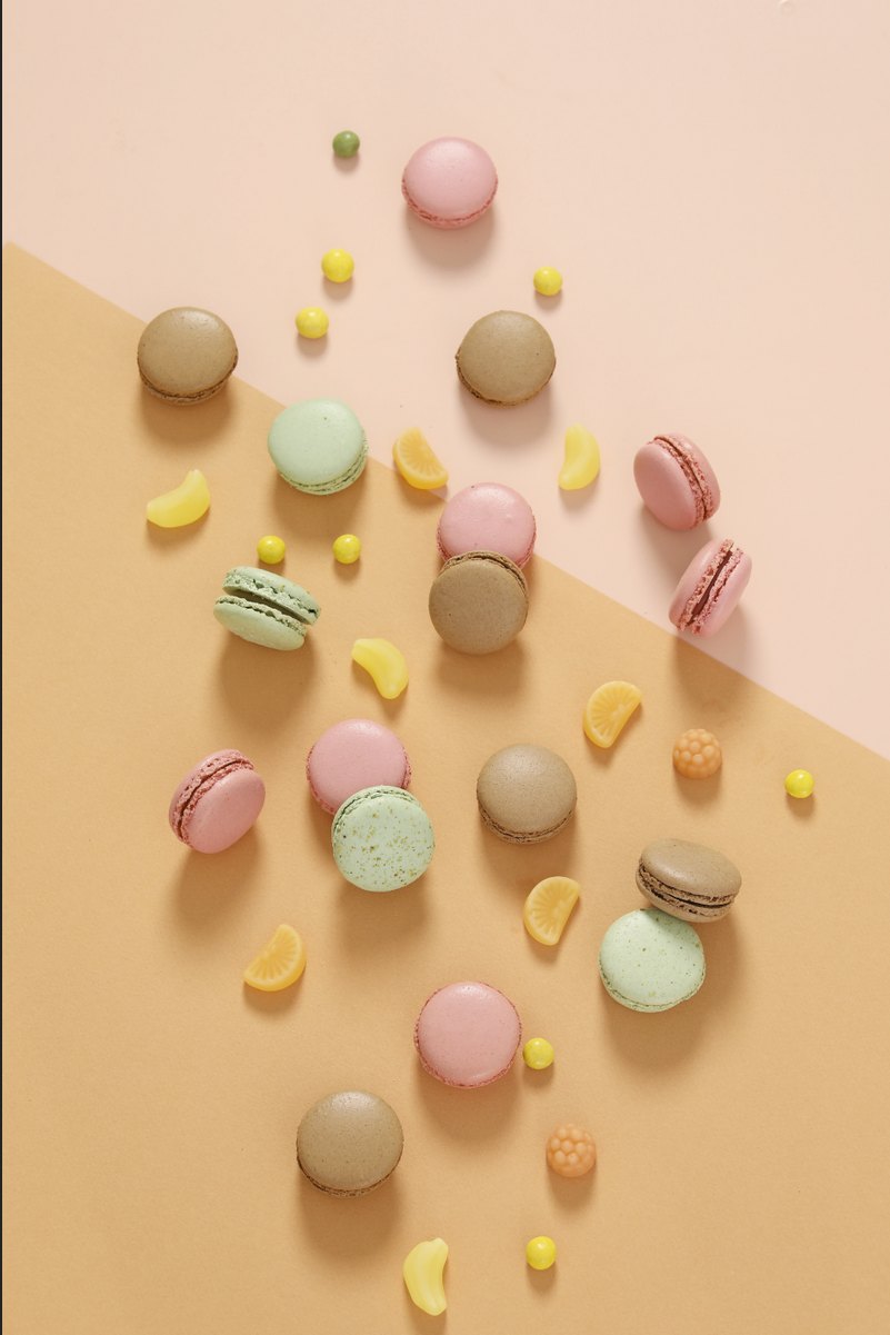 Macarons und Bonbons verstreut auf pastellfarbenem Hintergrund