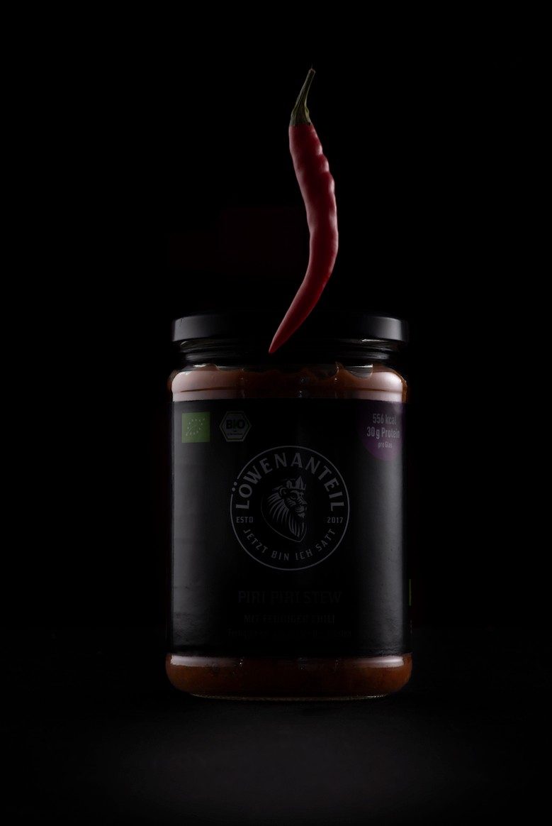 Dunkles Saucenglas mit schwebender roter Chilischote vor schwarzem Hintergrund