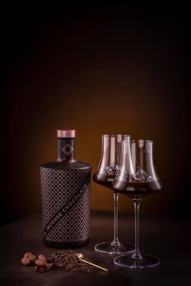 Schwarze Likörflasche mit Rautenmuster und zwei Gläser mit Schokoladenlikör vor dunklem, warmem Hintergrund