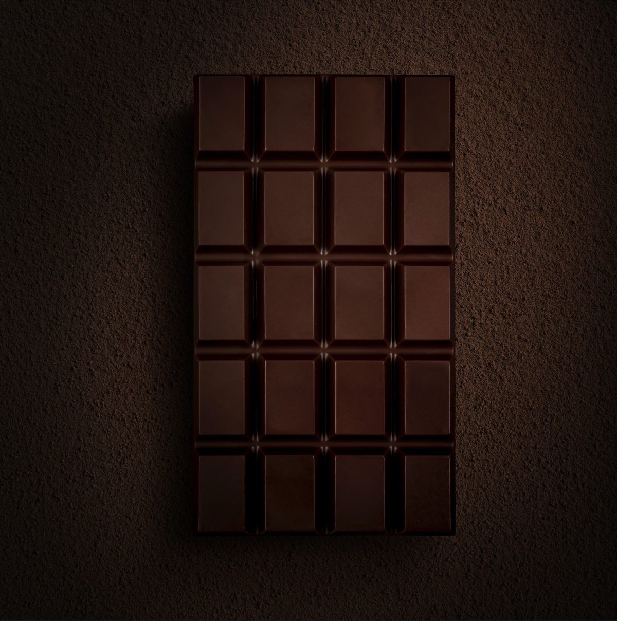 Dunkle Schokoladentafel in Low-Key-Licht auf braunem Kakaountergrund von oben