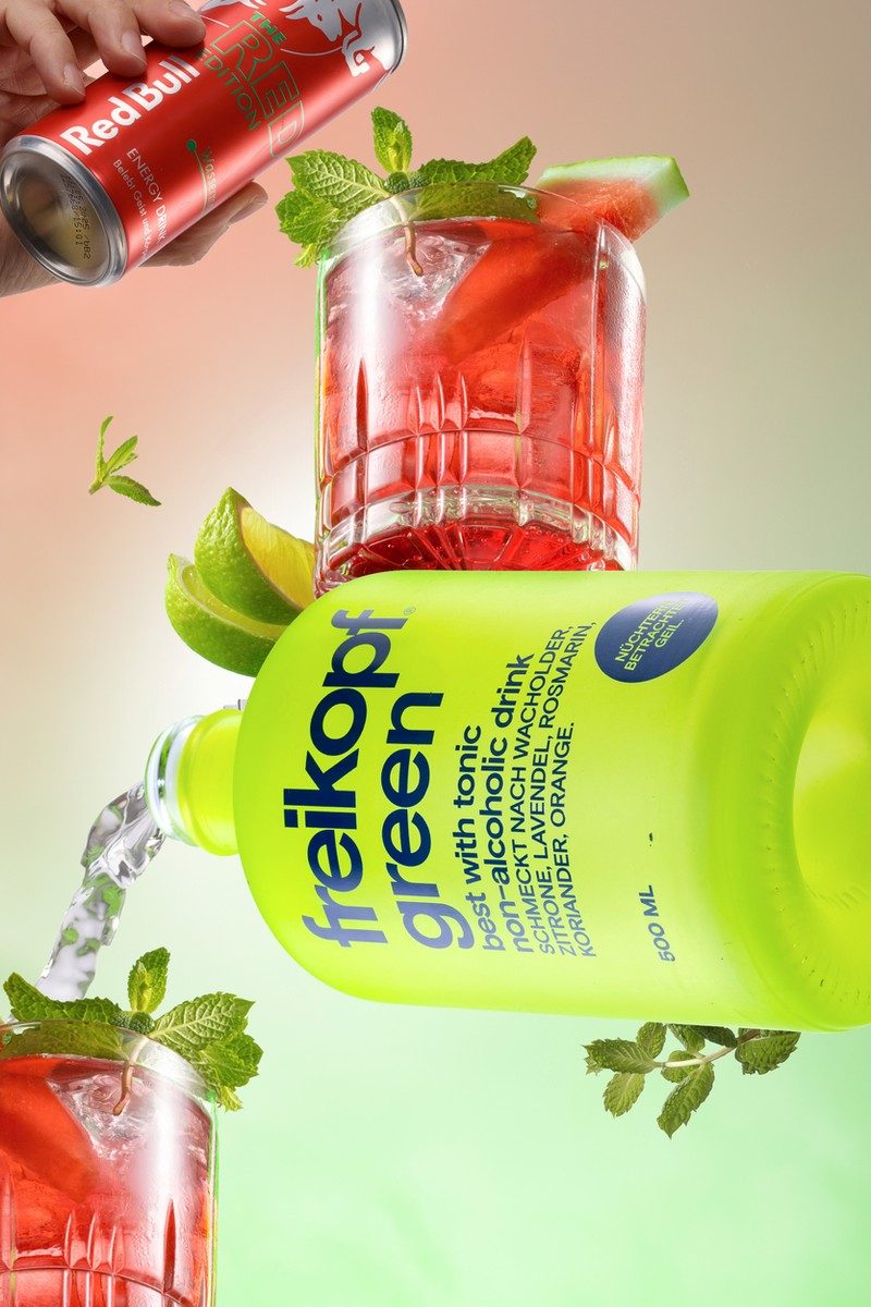 Schwebende grüne Getränkeflasche mit roten Drinks, Minze und Limette vor rosa-grünem Farbverlauf