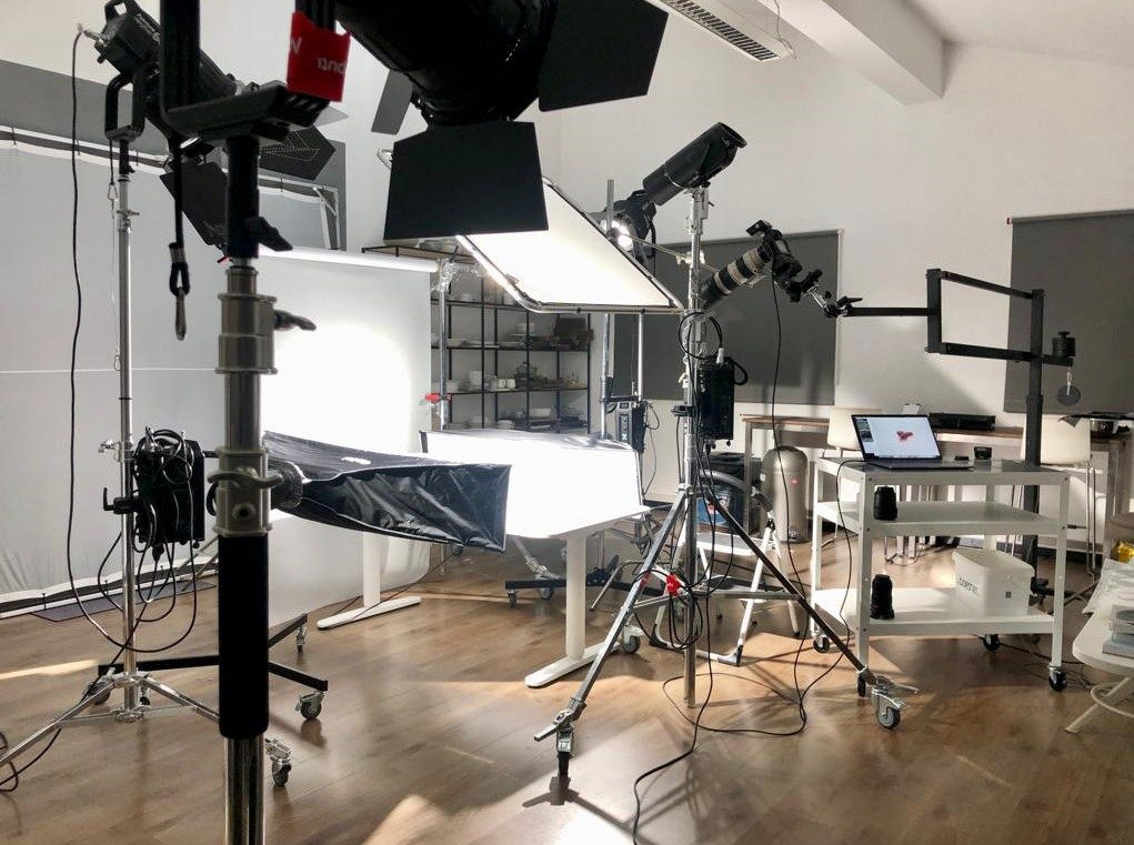 Fotostudio mit Lichtformern, Aufnahmetisch und Kamera samt Laptop-Arbeitsplatz