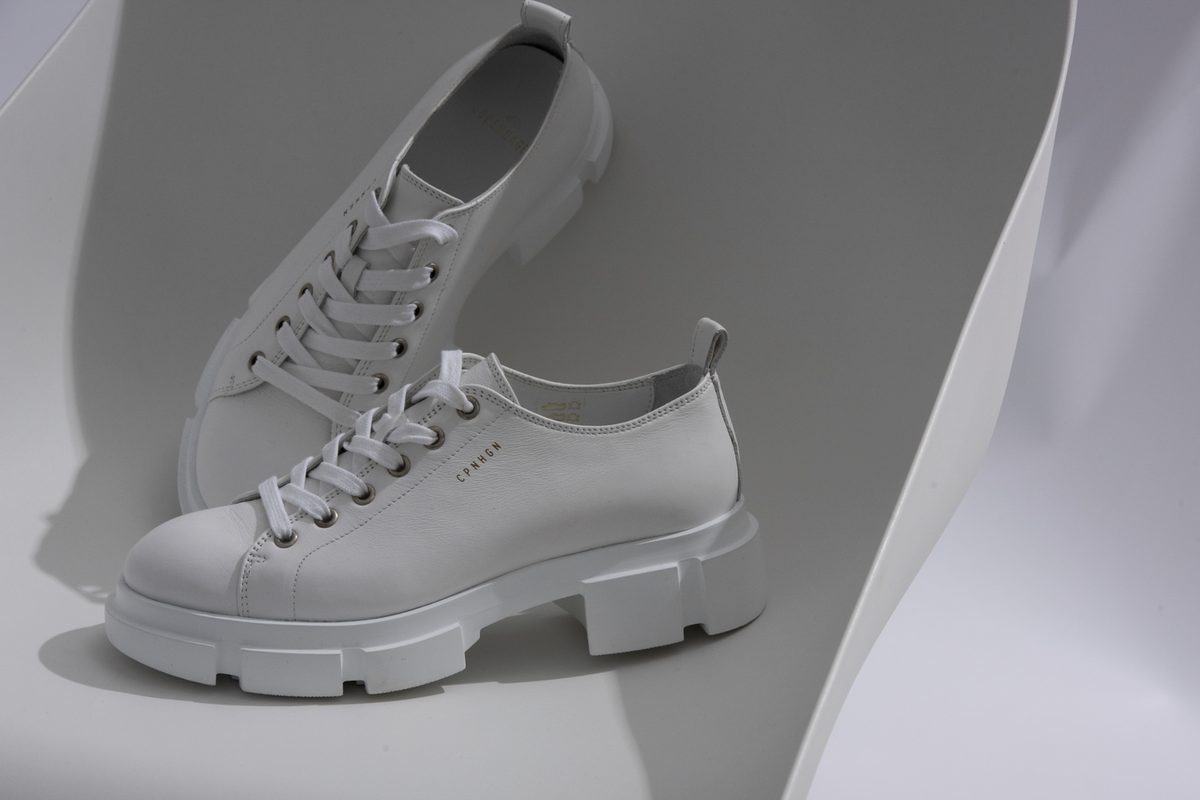 Zwei weiße Leder-Sneaker mit Plateausohle auf gebogenem weißem Untergrund