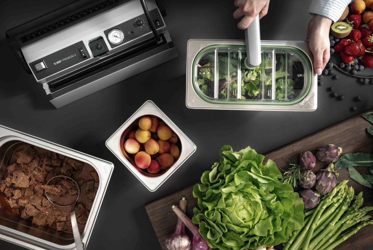 Aufsicht auf Vakuumiergerät, Behälter mit Salat und frische Zutaten auf dunkler Fläche