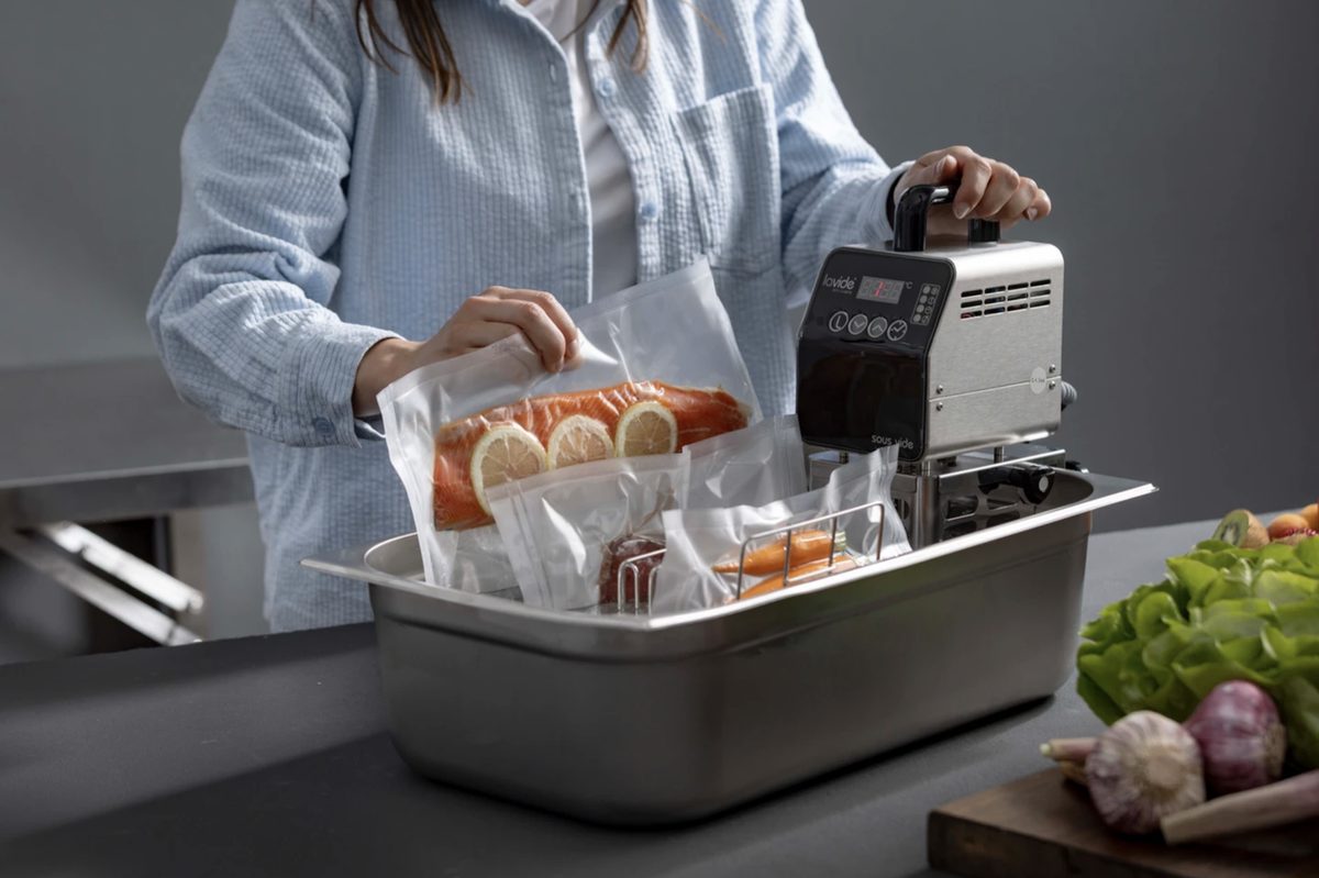 Frau legt vakuumierten Lachs in ein Wasserbad mit Sous-vide-Stick