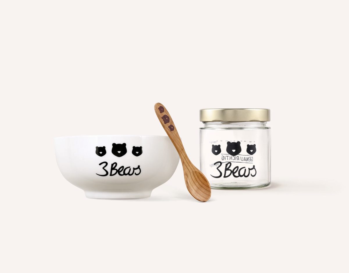 Weiße 3Bears Schale, Holzlöffel und Glas mit Schraubdeckel vor cremefarbenem Hintergrund