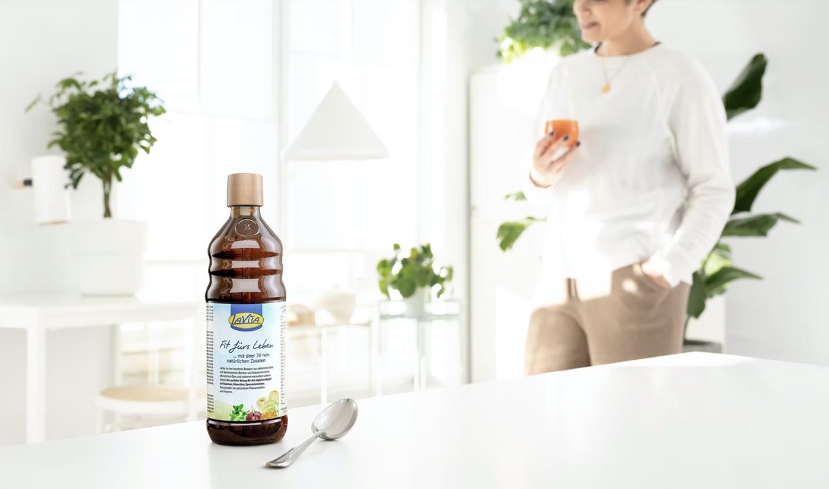 LaVita Flasche mit Löffel auf weißer Tischplatte, im Hintergrund unscharf eine Frau