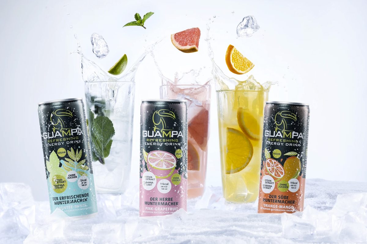 Drei Guampa Energy Drink Dosen vor Gläsern mit Eis, Früchten und Wasserspritzern