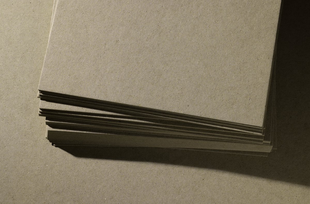 Gestapelte graubeige Kartonbogen mit sichtbarer Papierstruktur und aufgefächerten Kanten